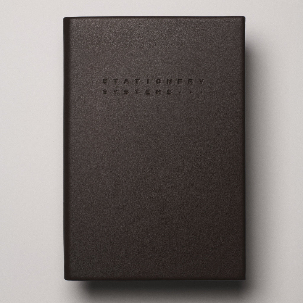 Dark brown notebook with 'Stationery Systems' branding on a beige background