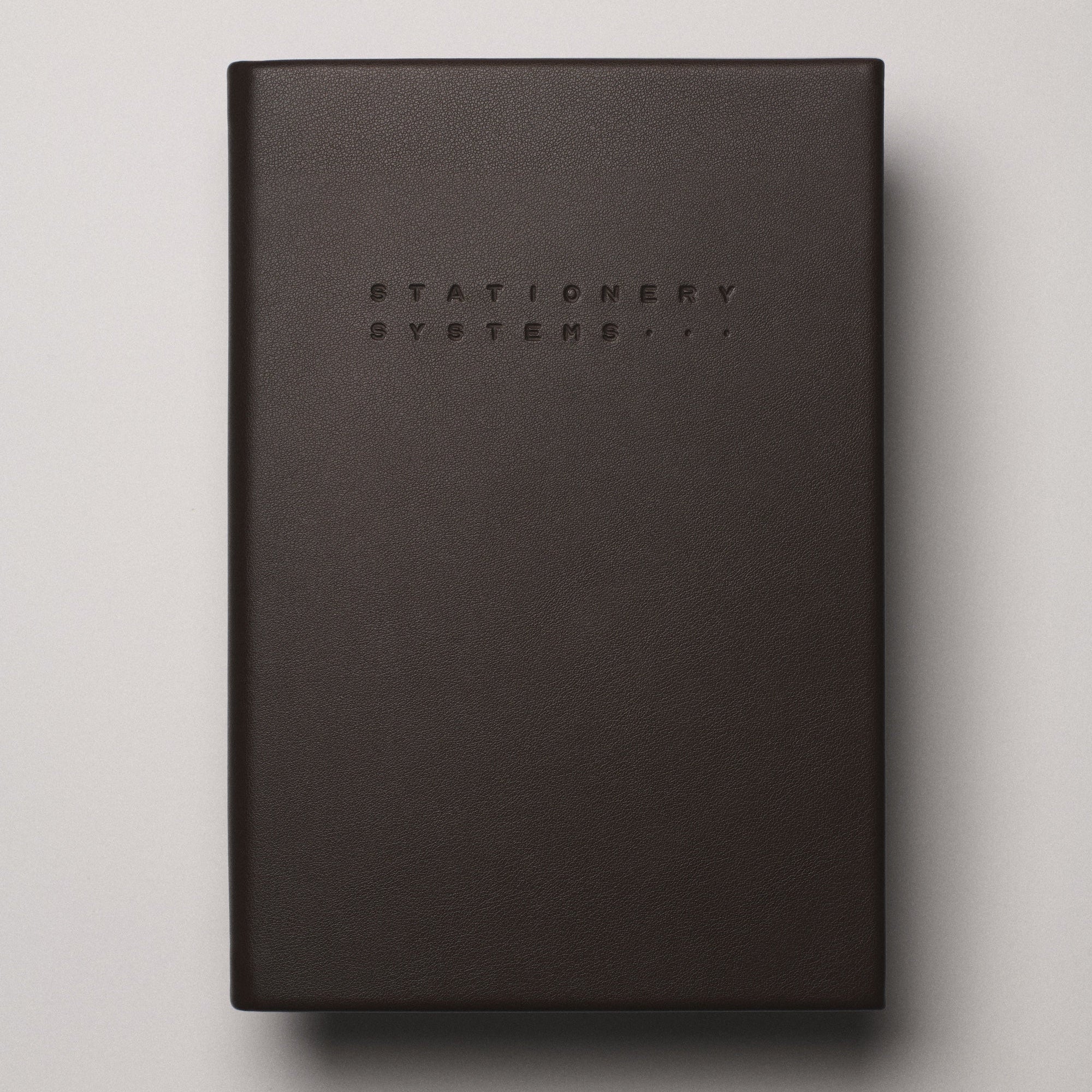 Dark brown notebook with 'Stationery Systems' branding on a beige background